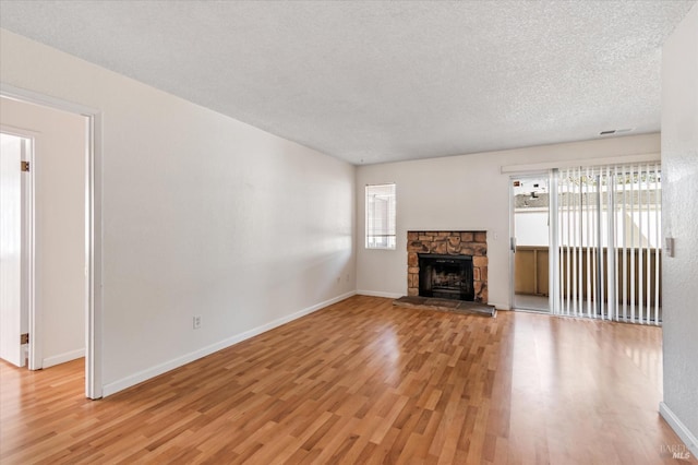 unfurnished living room with a textured ceiling, visible vents, a fireplace, light wood-type flooring, and baseboards