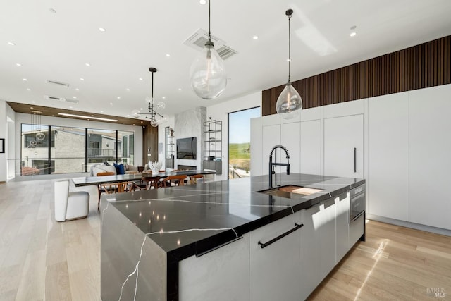 kitchen with open floor plan, modern cabinets, a large island with sink, a sink, and light wood-style flooring