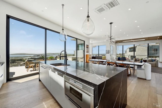 kitchen featuring a sink, light wood-style floors, open floor plan, a large island with sink, and modern cabinets