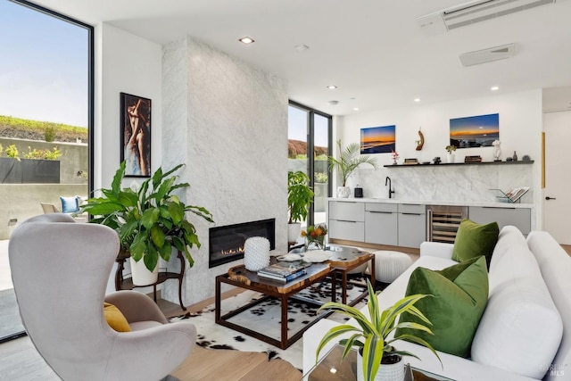 living area featuring wine cooler, a fireplace, a wall of windows, wet bar, and light wood finished floors