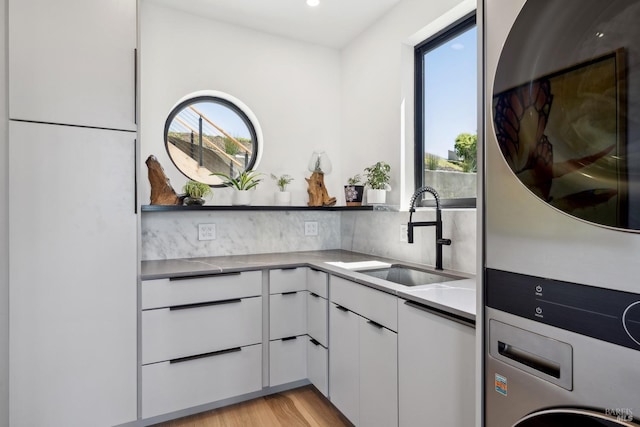 bar featuring decorative backsplash, stacked washer / dryer, oven, a sink, and light wood finished floors
