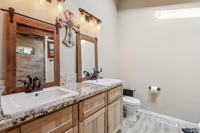 bathroom with toilet, double vanity, wood finished floors, baseboards, and a shower