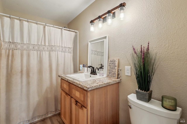 bathroom with vanity, toilet, a textured wall, and curtained shower
