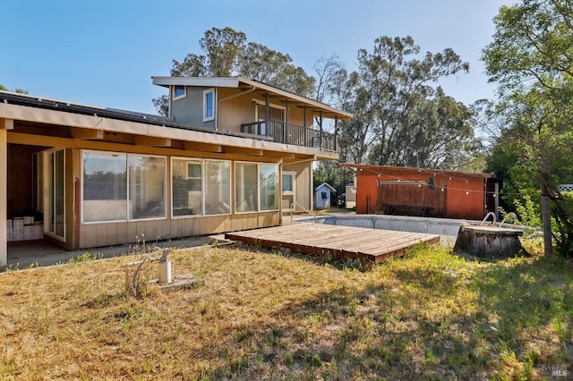 back of property featuring a deck, a sunroom, and a lawn