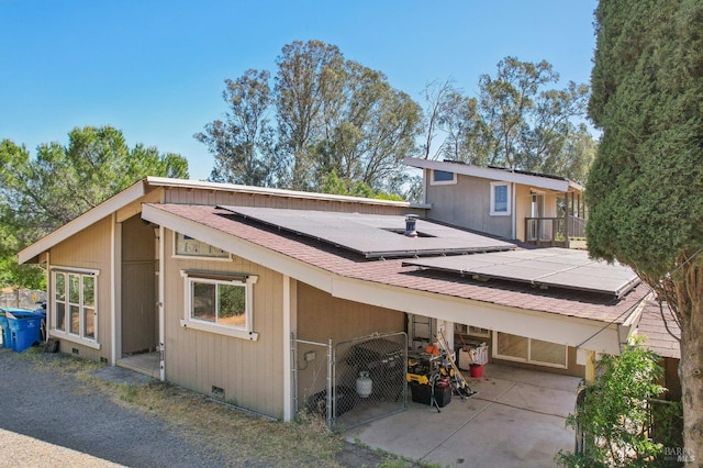 back of property with solar panels, roof with shingles, a carport, and crawl space