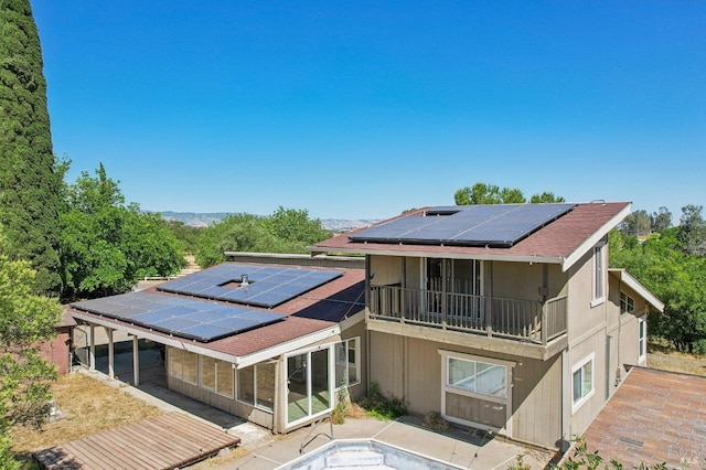 rear view of property with a sunroom, roof mounted solar panels, a balcony, and a patio area