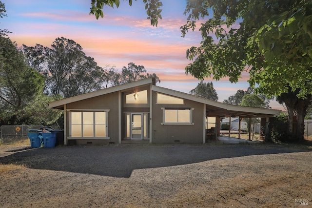 back of property featuring dirt driveway, an attached carport, and fence