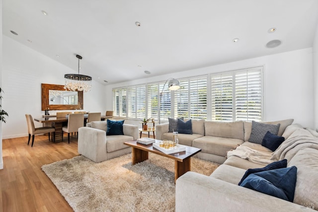 living room featuring light wood finished floors, a notable chandelier, and vaulted ceiling