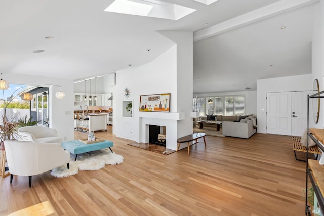 living area featuring beamed ceiling, high vaulted ceiling, a skylight, and light wood-style flooring