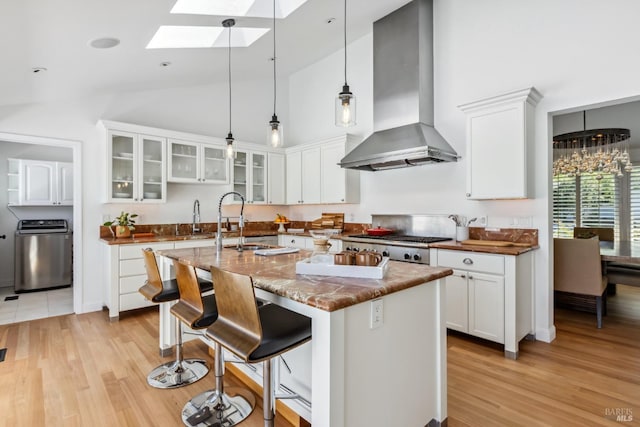 kitchen with a skylight, glass insert cabinets, light wood finished floors, and wall chimney exhaust hood
