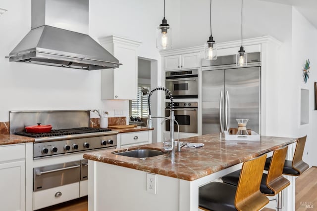 kitchen with wall chimney range hood, white cabinets, appliances with stainless steel finishes, dark stone countertops, and a warming drawer