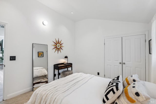 bedroom with a closet, baseboards, light wood finished floors, and vaulted ceiling
