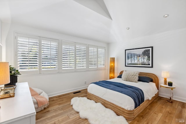 bedroom with baseboards, visible vents, light wood-type flooring, and lofted ceiling