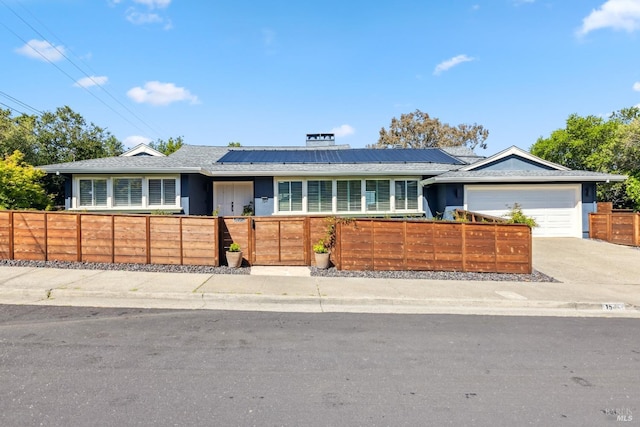 ranch-style home featuring driveway, a fenced front yard, solar panels, a garage, and stucco siding
