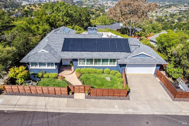 view of front facade with roof with shingles, a garage, concrete driveway, solar panels, and fence private yard