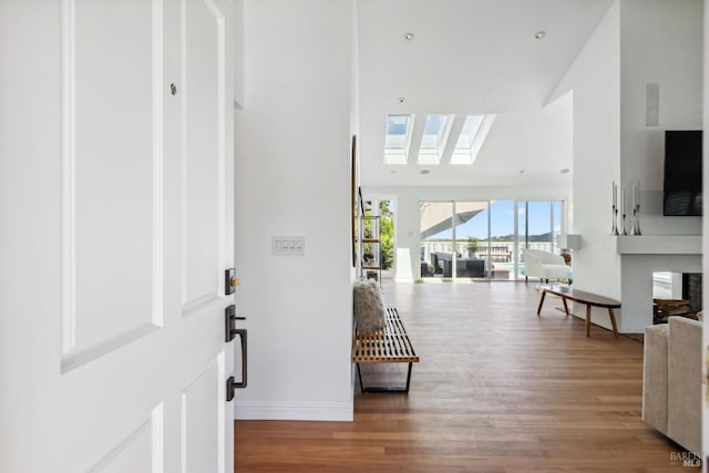 foyer featuring a skylight, baseboards, a high ceiling, and wood finished floors