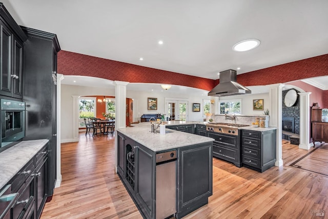kitchen with ornate columns, light wood-style flooring, dark cabinetry, and island exhaust hood