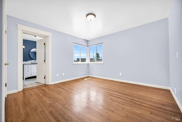 unfurnished bedroom featuring baseboards, wood finished floors, and connected bathroom