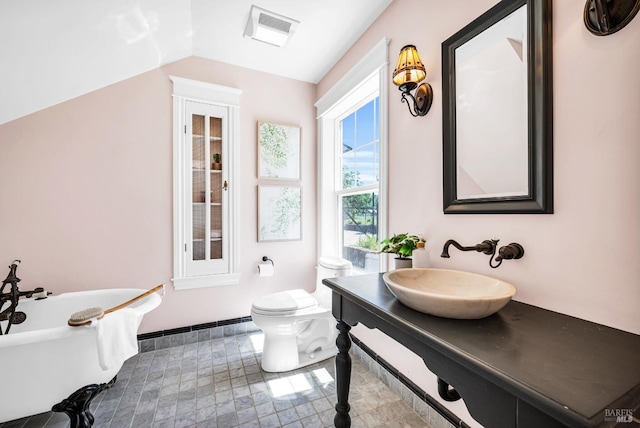 full bathroom featuring a freestanding bath, vanity, toilet, vaulted ceiling, and visible vents