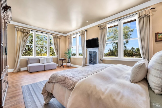 bedroom featuring baseboards, crown molding, light wood-style flooring, and a glass covered fireplace
