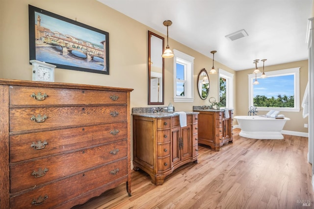 bathroom with a freestanding tub, two vanities, wood finished floors, and visible vents