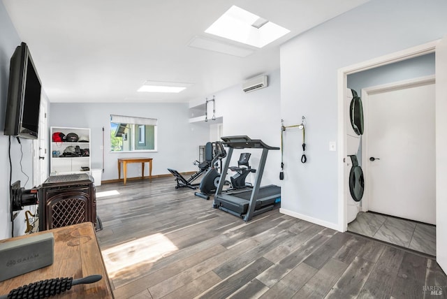 workout area with a skylight, stacked washer / drying machine, wood finished floors, baseboards, and an AC wall unit