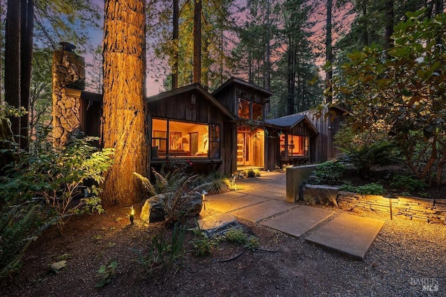 back of property at dusk featuring board and batten siding and a chimney