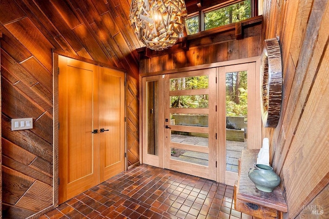 entrance foyer featuring lofted ceiling, wooden walls, wood ceiling, brick floor, and a notable chandelier