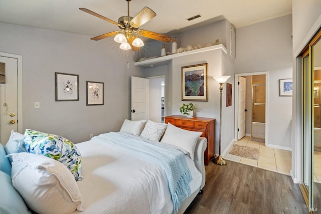 bedroom featuring a ceiling fan, visible vents, wood finished floors, baseboards, and ensuite bathroom