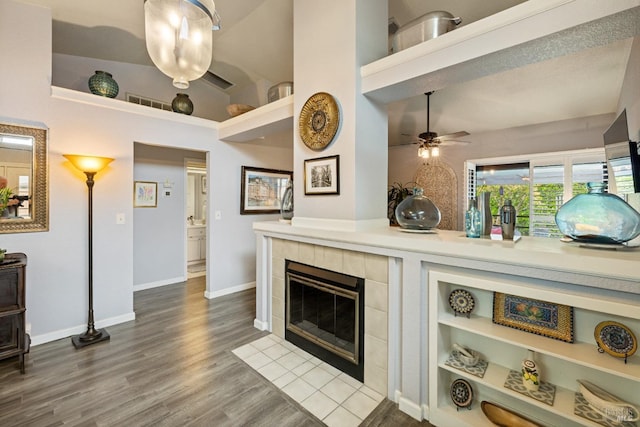 living area with dark wood-style flooring, a tiled fireplace, a ceiling fan, baseboards, and visible vents