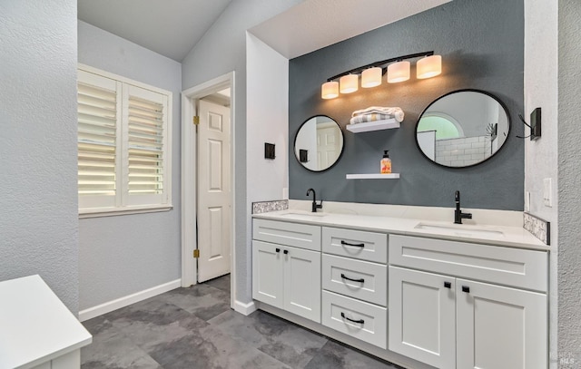 bathroom featuring double vanity, a textured wall, baseboards, and lofted ceiling