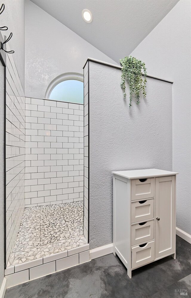 full bathroom featuring a stall shower, lofted ceiling, baseboards, and a textured wall
