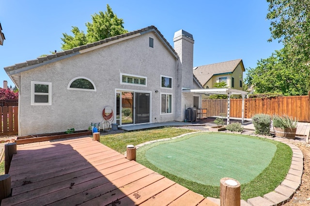 back of house featuring a putting area, fence, a wooden deck, a chimney, and stucco siding