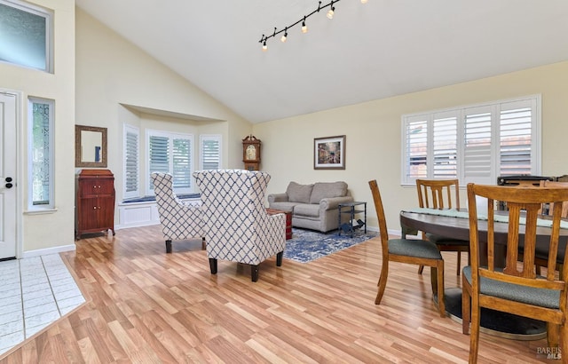 living area with light wood-type flooring, healthy amount of natural light, high vaulted ceiling, and baseboards