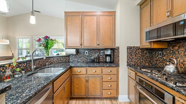 kitchen with a sink, brown cabinetry, stainless steel appliances, and lofted ceiling