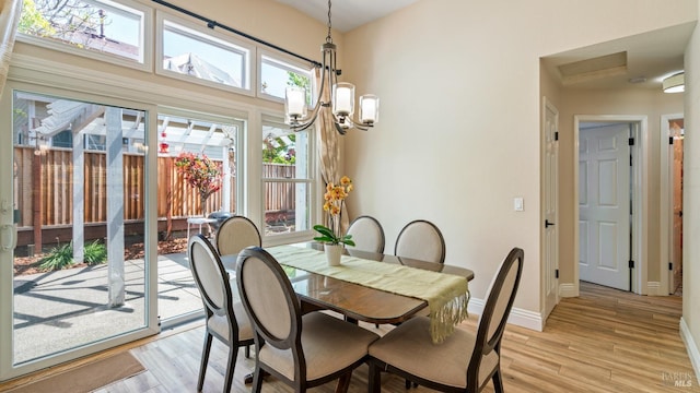 dining space featuring baseboards, light wood finished floors, a towering ceiling, and a chandelier