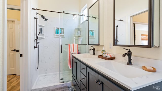full bathroom with a sink, a marble finish shower, double vanity, and wood finished floors