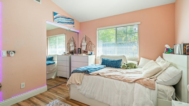 bedroom featuring baseboards, multiple windows, wood finished floors, and lofted ceiling