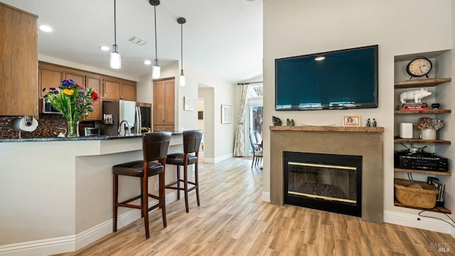 kitchen featuring brown cabinetry, a peninsula, stainless steel fridge, light wood-type flooring, and tasteful backsplash