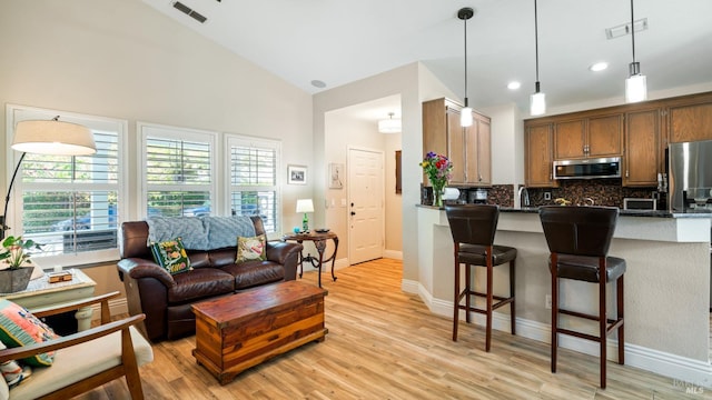 living area with baseboards, visible vents, high vaulted ceiling, and light wood-style floors