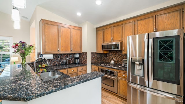 kitchen featuring brown cabinets, appliances with stainless steel finishes, a sink, light wood-style flooring, and a peninsula