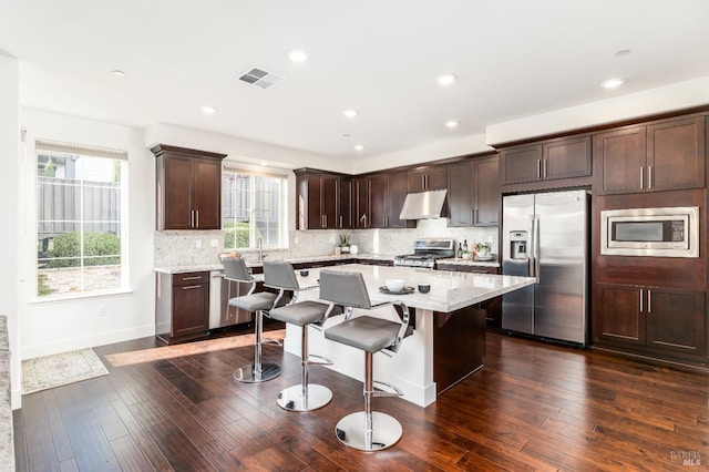 kitchen featuring dark brown cabinets, a kitchen breakfast bar, stainless steel appliances, under cabinet range hood, and a kitchen island