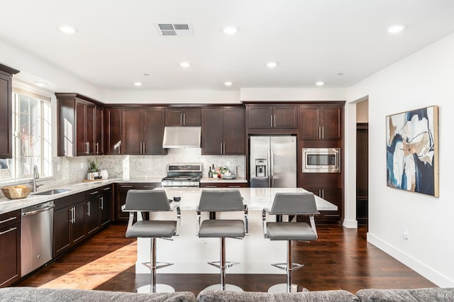 kitchen featuring dark brown cabinets, a center island, stainless steel appliances, under cabinet range hood, and visible vents