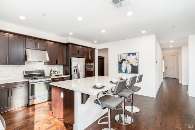 kitchen featuring light stone countertops, stainless steel appliances, under cabinet range hood, visible vents, and a kitchen island