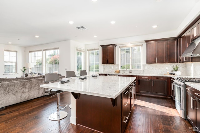 kitchen featuring a kitchen island, open floor plan, a breakfast bar area, stainless steel gas range, and light stone counters