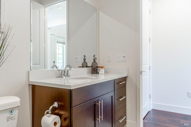 half bath with vanity, baseboards, toilet, and wood finished floors