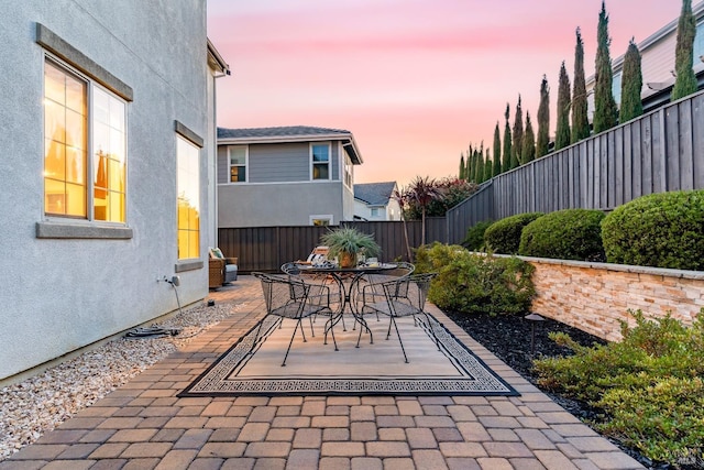 patio terrace at dusk with a fenced backyard and outdoor dining space