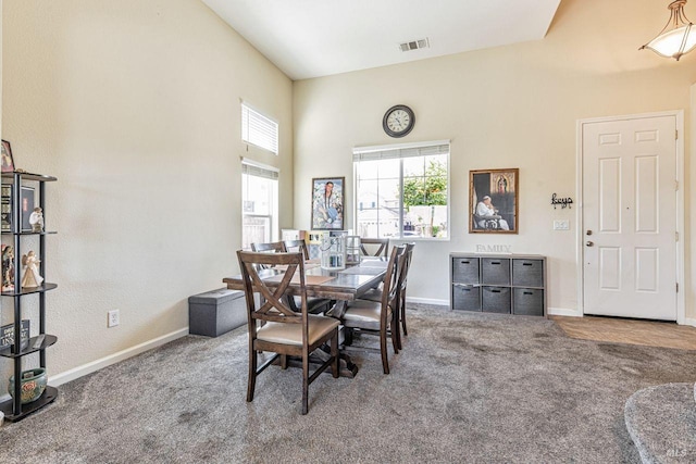 carpeted dining area with baseboards, a high ceiling, and visible vents