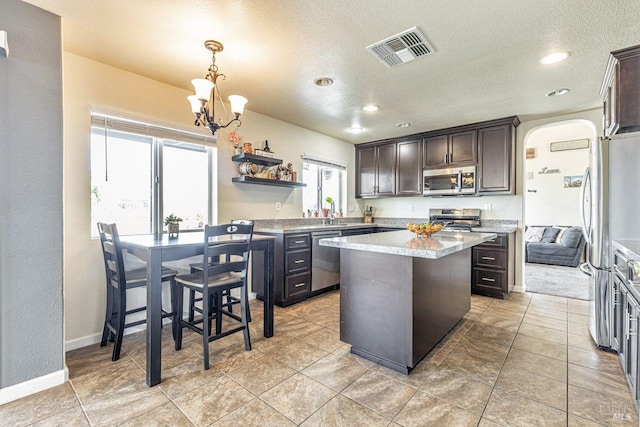 kitchen with open shelves, appliances with stainless steel finishes, an inviting chandelier, a center island, and visible vents