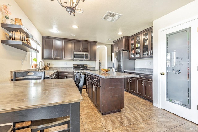 kitchen with dark brown cabinetry, visible vents, appliances with stainless steel finishes, arched walkways, and open shelves